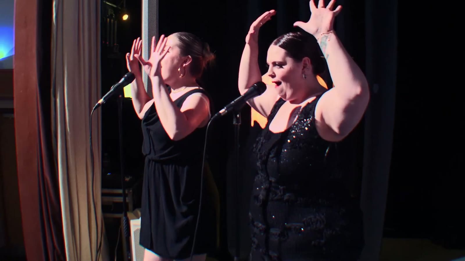 Lead vocalist and backing vocalist singing together at the microphones